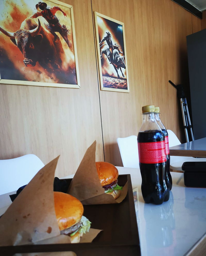 A table by the wall of bull posters, with a burger and a cola