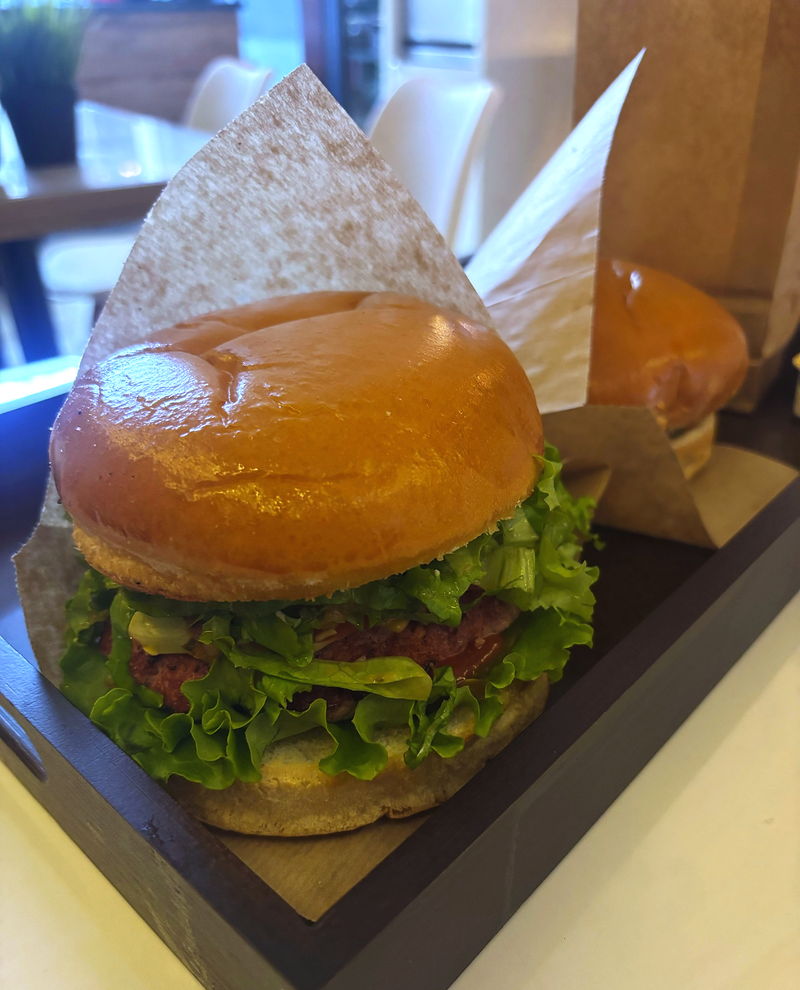 A burger with a glossy bun and lettuce on a wooden stand