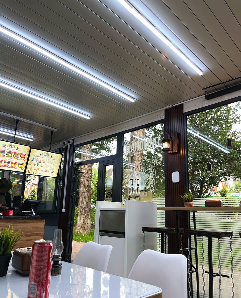 The room with long linear lights, a wooden ceiling and windows onto the street
