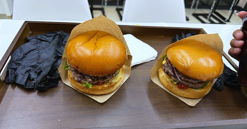 Two burgers on a tray beside disposable gloves