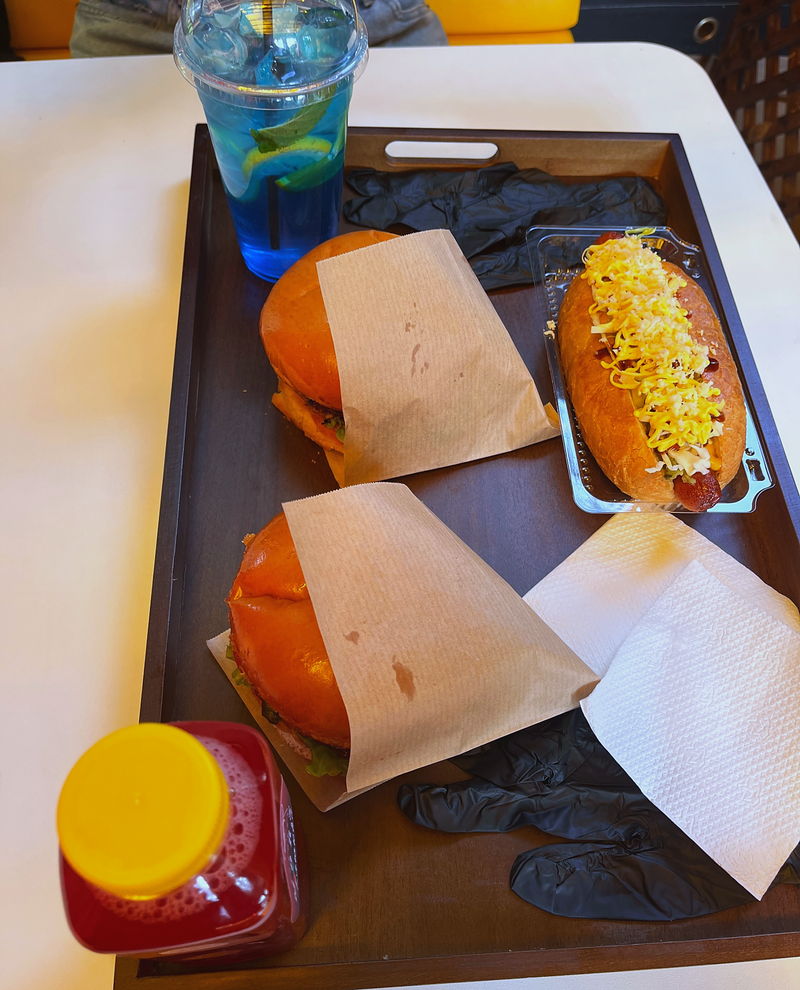 A tray with a hot dog, potato wedges and sauces in pots