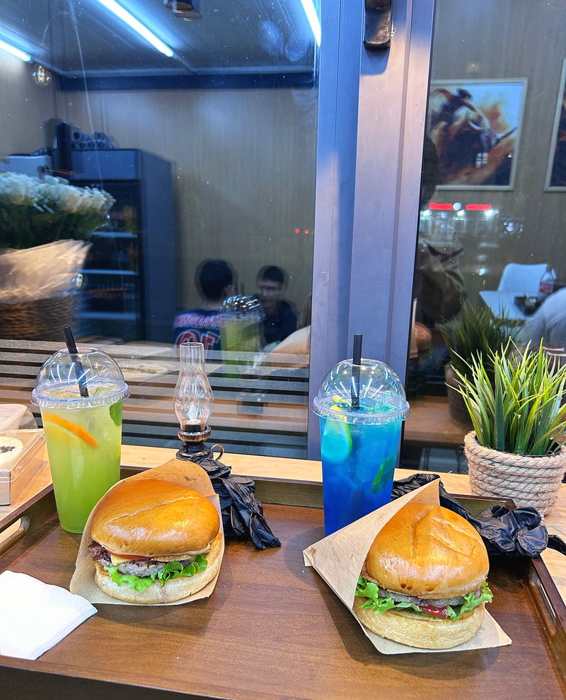 Two burgers and a blue lemonade on a table by the window