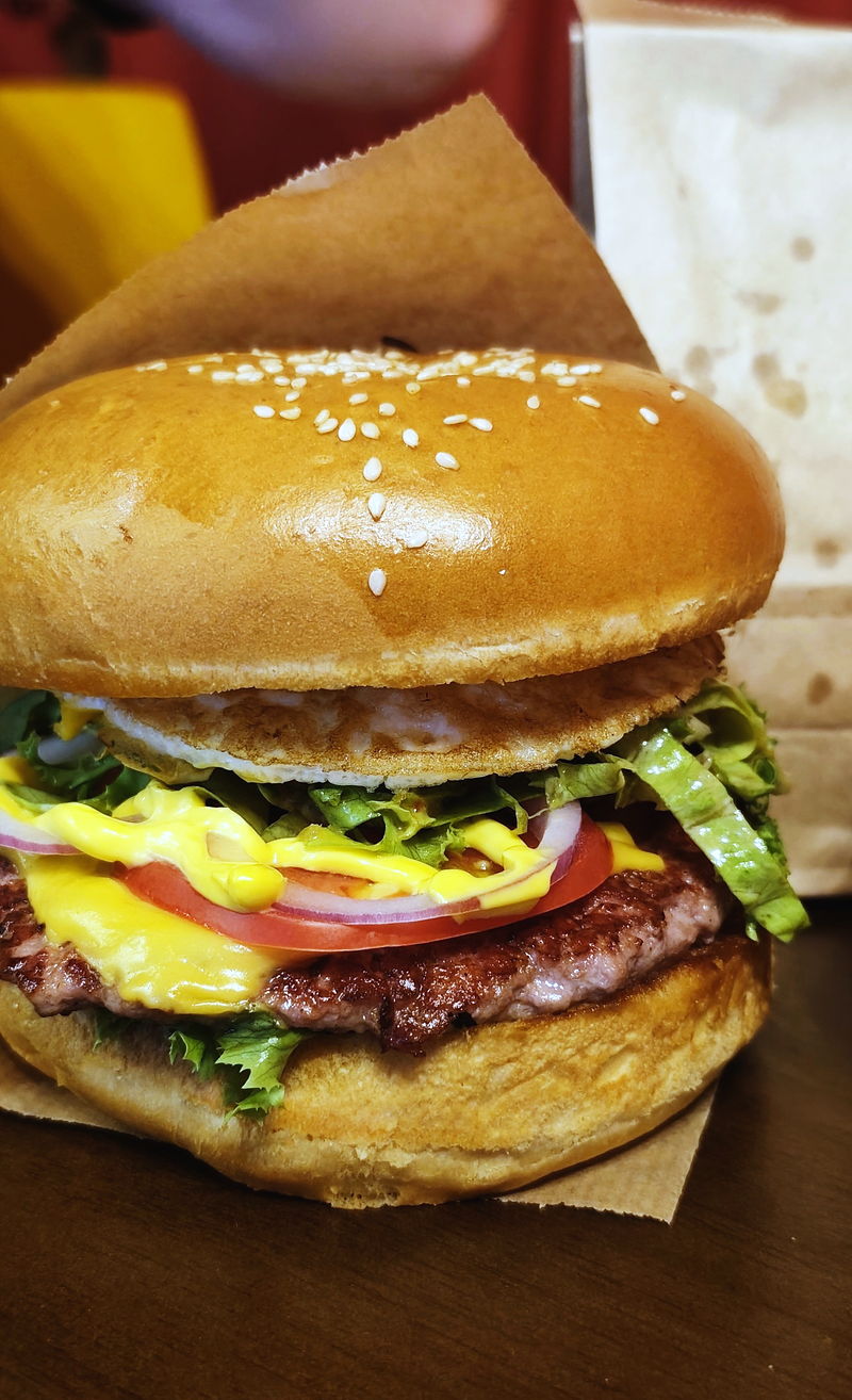 A close-up of a burger with a sesame bun, cheese and tomato