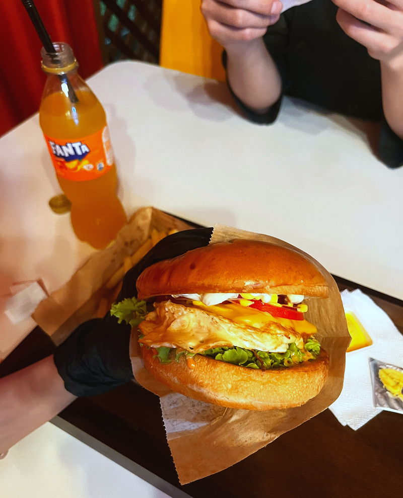 A burger in hand with an orange lemonade