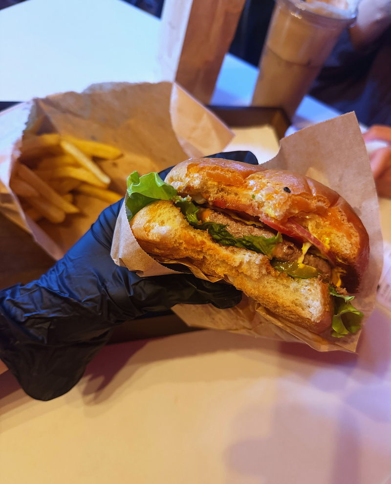 A close-up of a burger held in a glove, its bun glossy and deep orange