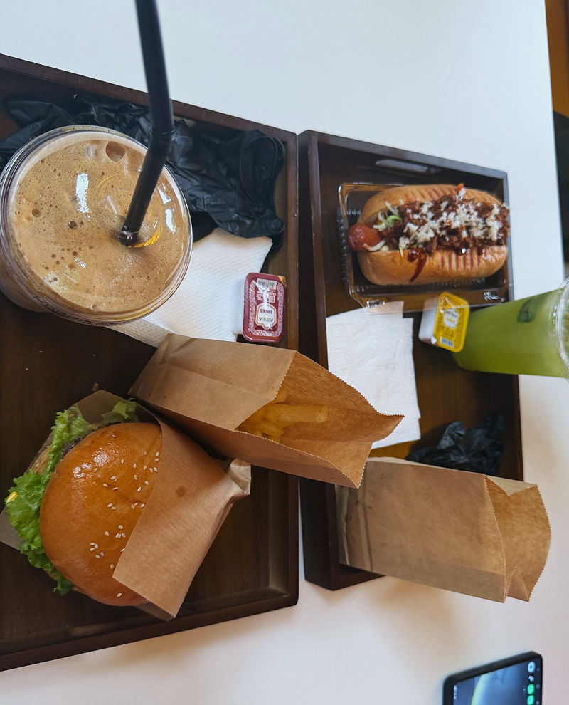 A combo on a tray: burger, hot dog, kraft bags and an iced latte